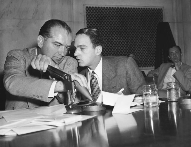  Sen. Joseph McCarthy covers the microphones with his hands while having a whispered discussion with Roy Cohn, his chief counsel, during a committee hearing on April 26, 1954, in Washington. | AP Photo